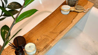 Wooden tray with a candle, diffuser, and brush on a bathtub ledge.